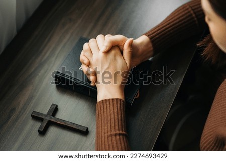 Hands together in prayer to God along with the bible In the Christian concept and religion, woman pray in the Bible on the wooden table

