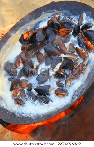 Cooking mussels on an open fire, in a steel pan, according to a French recipe, with the addition of wine and spices. Cooking fresh mussels on the seashore.