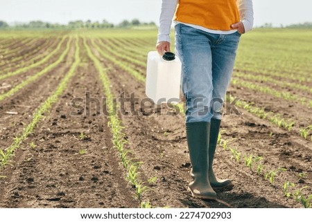 Corn crop protection concept, female farmer agronomist holding jerry can container canister with pesticide, selective focus