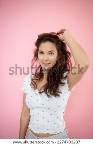 pretty young woman with black sunglasses with flowered shirt stands in front of pink background