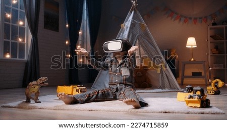 Cute little boy wearing pajamas is diving into virtual reality world before bedtime, using vr 3d headset, playing video games - modern technology concept  Royalty-Free Stock Photo #2274715859
