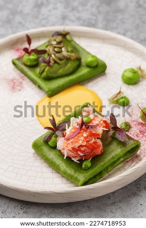 Colorful green crepes or blini with crab meat, avocado mousse and hollandaise sauce, decorated with micro greens and pumpkin seeds. Gourmet snack. Fine dining. Close up view Royalty-Free Stock Photo #2274718953