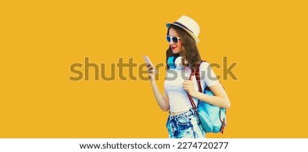 Summer colorful portrait of stylish modern young woman listening to music in headphones with smartphone on orange background
