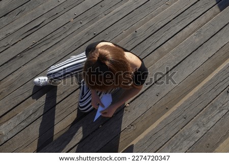 The girl sits on the old wooden stairs and folds a paper airplane