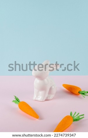 White rabbit with carrots on bright background. Minimal pastel pink and blue Easter holiday concept.