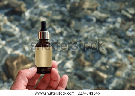 Amber Bottle of serum in hands against a background of sea water Mockup of a cosmetic product. Skin care essence for beautiful, healthy skin. Empty label