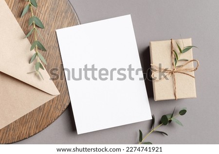 Blank greeting card mockup with gift box and envelope on wooden background