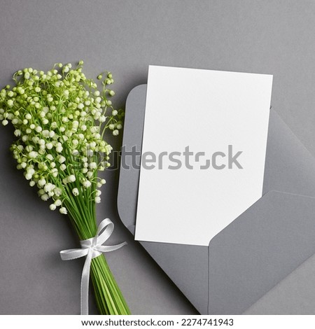 Blank wedding invitation card mockup with white lily of the valley flowers on grey background