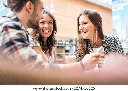 Multiracial group of friends having a coffee together - Two women and a man at cafe, talking, laughing and enjoying their time - Lifestyle and friendship concepts with real people models Royalty-Free Stock Photo #2274750525