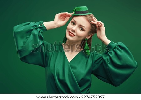 Cute young woman in a green leprechaun hat and a green dress for a Saint Patrick's Day. Studio portrait on a green background. 