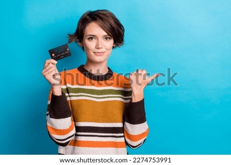 Photo of positive cute woman dressed striped pullover pointing thumb empty space rising credit card isolated blue color background