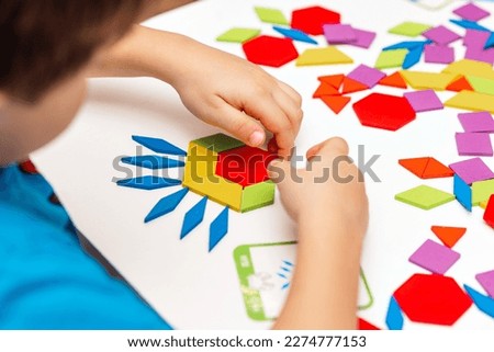 Close up of kid hands playing bright wooden tangram toy. The child collects a pattern of wooden bars. Creative baby make new forms.