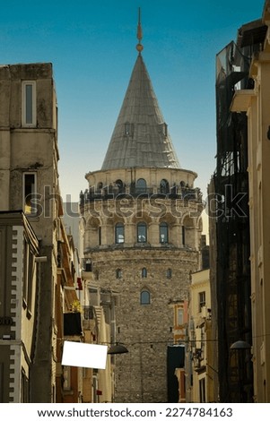 The view of the Galata tower from among the buildings, Galata Tower and blank white signboard on the street. Vertical photo. Istanbul's history, one of the tourist attractions. Blue sky. Copy space
