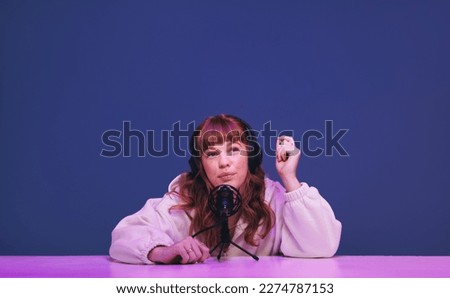 Woman with ginger hair whispering into a microphone as she records an asmr podcast. Female content creator hosting a relaxing audio broadcast for her social media fanbase. Royalty-Free Stock Photo #2274787153