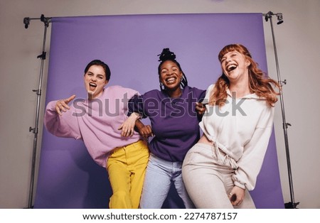 Three multicultural friends dancing and having fun in casual clothing. Group of female friends celebrating and having a good time against a purple background. Best friends making happy memories. Royalty-Free Stock Photo #2274787157
