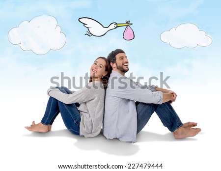 young attractive Hispanic couple on floor, pregnant woman sitting together handsome husband and flying stork bringing baby in pregnancy and family growth concept Royalty-Free Stock Photo #227479444