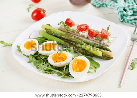 Green asparagus with boiled eggs and sandwich cream cheese on a white plate.