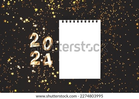 Empty notepad mockup, glowing stars confetti and 2024 golden numbers on a black background. New Year wish list concept.