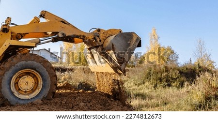 A large yellow wheel loader aligns ground for a new building. Land preparation for the auction or sale. Plot leveling and adding sand for construction. Banner. Copy space. Special transport. Closeup.