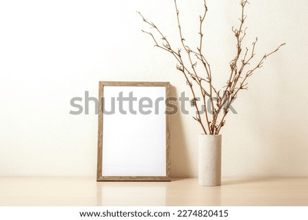 Template with photo frame on a wooden desk. Dried branches in the vase.