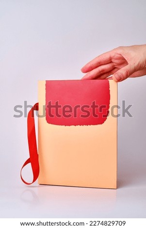 A woman holds a small gift box in her hand on a light background. Postal services, delivery. Mock - up packaging. Gift box, gift. Box close-up. Empty packaging, empty space