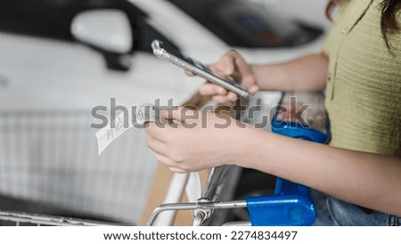 Women use mobile phone to calculate bill after shopping at the supermarket, Close up of hand checking long grocery receipt, she is using a budgeting and money saving mobile app Royalty-Free Stock Photo #2274834497