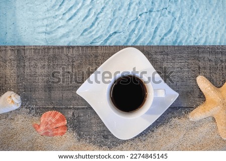 Coffee cup seen from above on a wooden pavement above a pool with a starfish. Ambiance vacation in summer.	