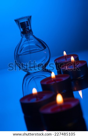 Burning candles and perfume bottle with reflection