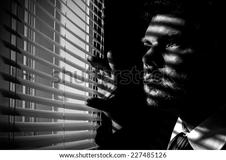 Man looks through blinds from a dark room Royalty-Free Stock Photo #227485126