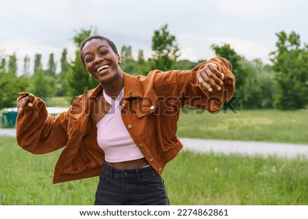 A young African American woman with short hair is seen dancing and laughing in a public park during springtime - black girl wearing casual clothes, exuding joy, liveliness, and youthfulness Royalty-Free Stock Photo #2274862861