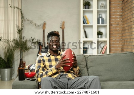 Young African man watching sport match on television and supporting his favorite team. Happy man enjoying victory, watching sports competition on tv.
