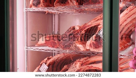 Big piece of red dry aged beef rib eye at butcher in a glass store window vitrine. Matured beef rib in a showcase in masket. Royalty-Free Stock Photo #2274872283