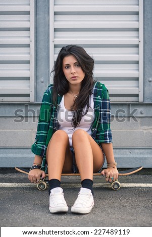Teenager sit on skateboard outdoors in a urban background.