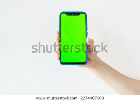 Mockup image, girl holding smartphone with blank green screen on white wall. Selective focus, noise. Ready mockup for designers