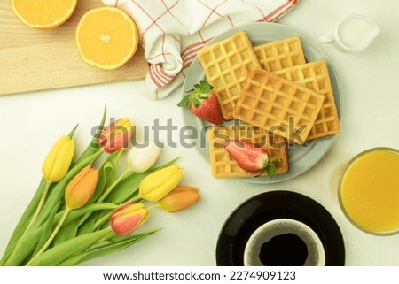 Freshly baked homemade waffles on a plate. Homemade waffles with strawberries. Tulips and coffee waffles. Side view
