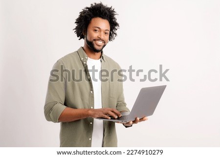 Smiling positive man holding laptop in hands and typing. Blogger making posts in social networks, chatting with followers. Indoor studio shot isolated on white background Royalty-Free Stock Photo #2274910279