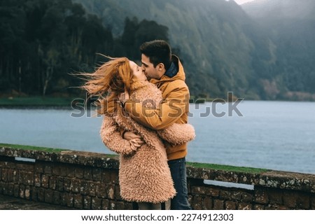 The guy kisses the girl and hugs near the lake and the mountains. close up Royalty-Free Stock Photo #2274912303