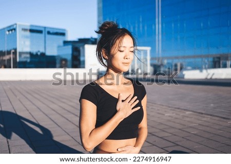 Mindfulned female yogi in tracksuit meditating in hatha pose enjoying relaxation and pranayama time at urban setting, concept of holistic healing and mental healthy lifestyle for feeling tranquility Royalty-Free Stock Photo #2274916947