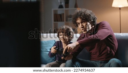 Cute authentic asian brothers with curled hair enjoying their together time, playing football video games in front of tv, parent and son relaxing with their hobby 
