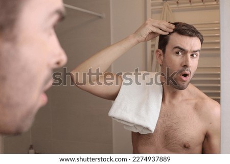 Surprised looking man observing his hairline in the mirror  Royalty-Free Stock Photo #2274937889