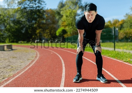 Asian sportsman tired after running and active physical exercise, man taking breath and rest on sunny day in stadium, overtired after running. Royalty-Free Stock Photo #2274944509