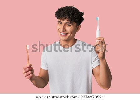 A young man compares manual vs electric toothbrush for optimal dental care - weighing effectiveness, convenience, and cost. Royalty-Free Stock Photo #2274970591