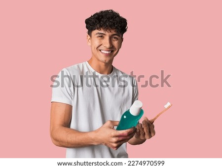 A young man promotes daily dental hygiene, holding a toothbrush and mouthwash for fresh breath, cavity-free teeth, and healthy gums. Royalty-Free Stock Photo #2274970599
