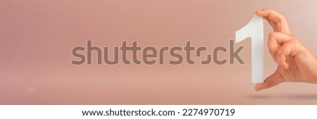 Number one in hand. A hand holds a white number one on a red background with copy space. Concept with number one. 1 percent rate, birthday, first or winner. Royalty-Free Stock Photo #2274970719