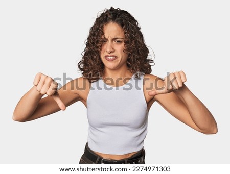 Radiant young woman with stunning curls showing thumb down and expressing dislike.