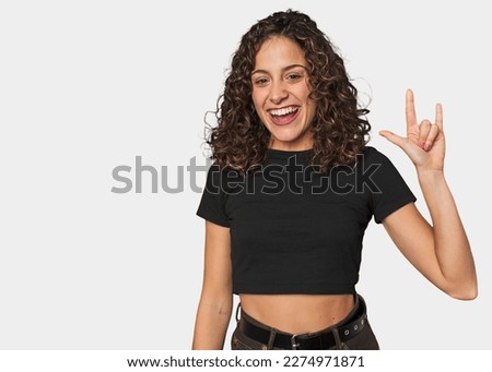 Radiant young woman with stunning curls showing a horns gesture as a revolution concept.