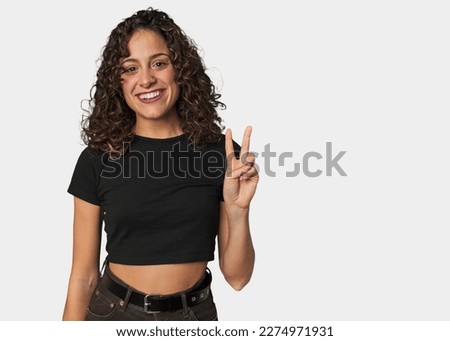 Radiant young woman with stunning curls showing victory sign and smiling broadly.