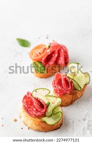 Bruschetta with sausage and vegetables on light gray background. Three of salami sandwiches as appetizer isolated close up. Vertical orientation Royalty-Free Stock Photo #2274977121