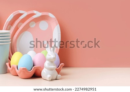 Cute paper cups and  plates in the shape of  eggs with  Easter eggs, candy and Easter Bunny. Happy Easter. Set of holiday disposable tableware and decorations for party or picnic.
