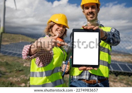 Two engineers at a solar power plant are holding tablet with blank screen for mock up